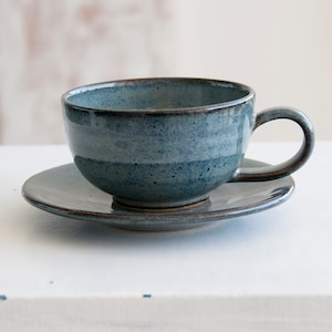 May include: A blue ceramic teacup and saucer set. The cup and saucer have a speckled glaze and a dark brown rim.