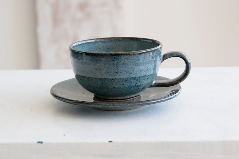 May include: A blue ceramic teacup and saucer set. The cup and saucer have a speckled glaze and a dark brown rim.