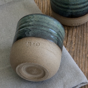 May include: Two ceramic mugs with a green glaze and a brown base. One mug has the initials "M+D" inscribed on the side.