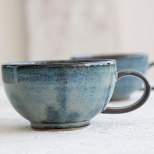 May include: Two blue ceramic mugs with a speckled glaze. The mugs have a rounded shape and a handle.