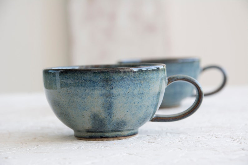 May include: Two blue ceramic mugs with a speckled glaze. The mugs have a rounded shape and a handle.