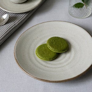 Puede incluir: Dos galletas verdes de matcha en un plato de cer&aacute;mica blanco con una superficie texturizada.