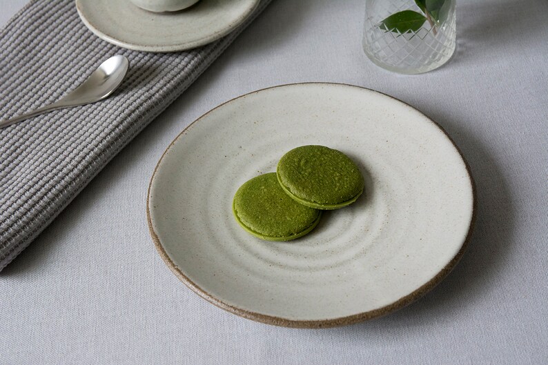Puede incluir: Dos galletas verdes de matcha en un plato de cer&aacute;mica blanco con una superficie texturizada.