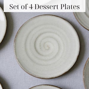 Puede incluir: Juego de cuatro platos de postre de cer&aacute;mica blanca con un dise&ntilde;o en espiral. Los platos tienen un borde marr&oacute;n.