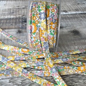 May include: A spool of yellow, pink and blue floral patterned ribbon. The ribbon is made of cotton and is approximately 1.2 cm wide.