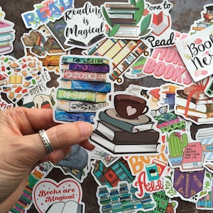 May include: A selection of book-themed stickers, featuring stacks of books, coffee cups, and phrases such as "Reading is Magical" and "Book Nerd." The stickers showcase diverse designs and colours, ideal for book enthusiasts and journaling.