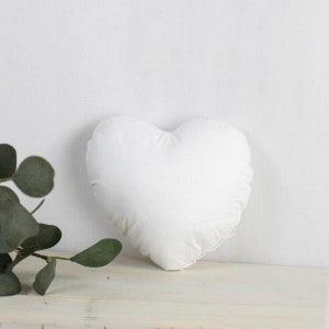 May include: A white heart-shaped pillow with a ruffled edge.