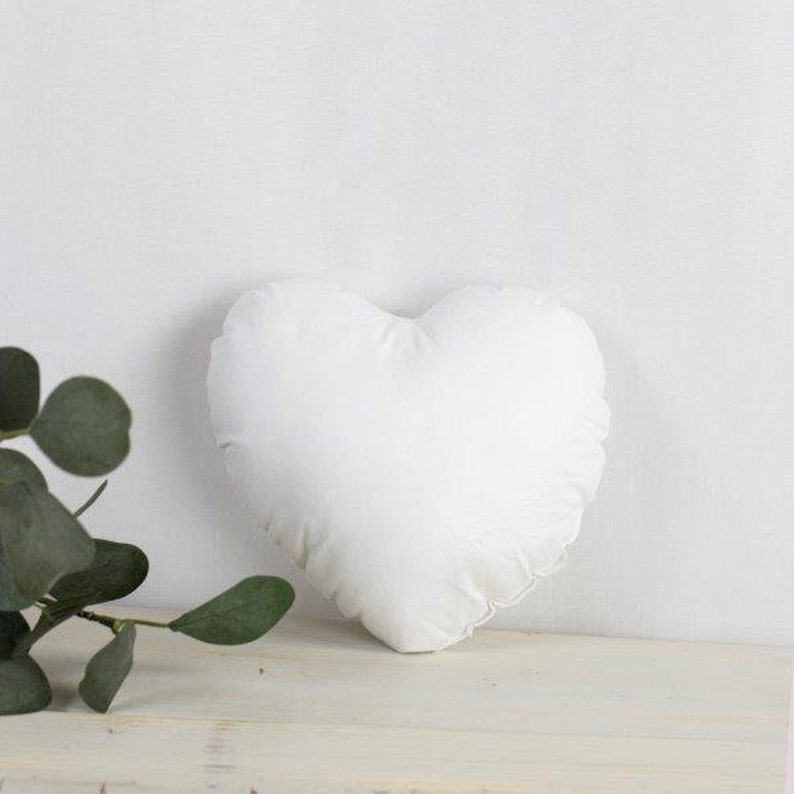 May include: A white heart-shaped pillow with a ruffled edge.