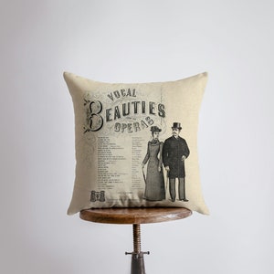 May include: A beige cushion with a vintage design featuring a couple in formal attire. The text on the cushion reads "Vocal Beauties from the Operas".