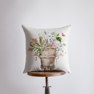 May include: A white pillow with a watercolor illustration of a terracotta pot filled with a bouquet of colorful flowers and a red butterfly.