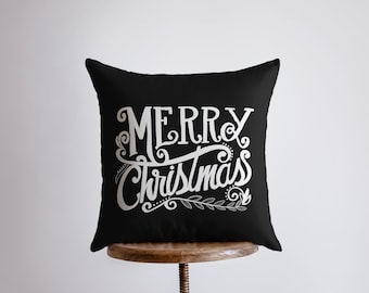 May include: Black throw pillow with white lettering that says "Merry Christmas" with a decorative flourish and a small sprig of leaves.