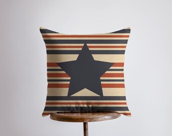 Op de afbeelding: Een decoratief kussen met een donkerblauwe ster op een achtergrond van beige, rode en donkerblauwe strepen.