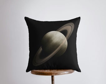 May include: A black throw pillow with a graphic of Saturn, a gas giant planet with rings, on a dark background.
