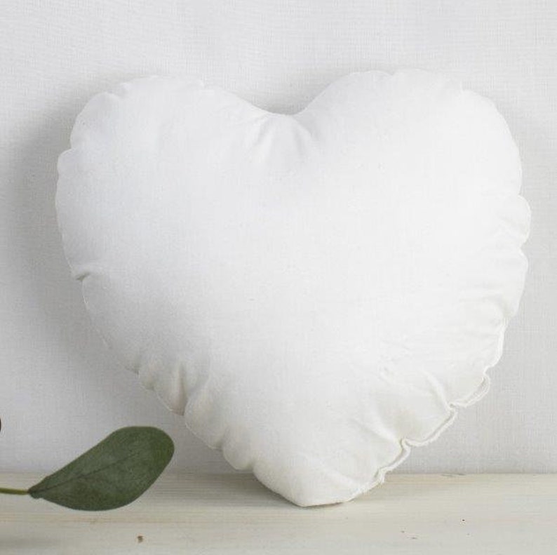 May include: A white heart-shaped pillow with a ruffled edge.