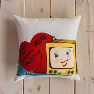Puede incluir: Una almohada blanca con un diseño vintage de San Valentín que presenta un corazón rojo con el texto "Tune in Channel Valentine Mine" y un televisor de dibujos animados con una cara sonriente.