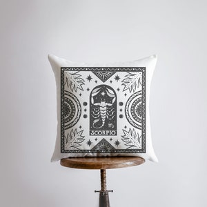 May include: White throw pillow with a black and white illustration of a scorpion with the text "Scorpio" and the astrological symbol for Scorpio.
