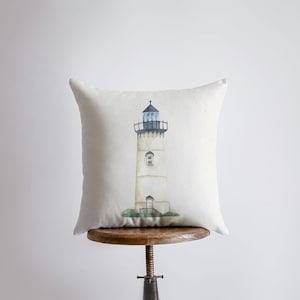 May include: A white pillow with a watercolor illustration of a lighthouse on a beige background.