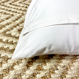 May include: A white pillowcase with a zipper closure. The pillowcase is lying on a woven rug.