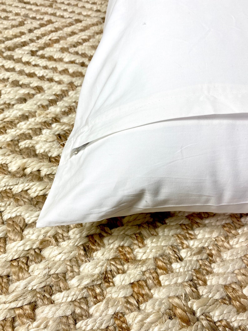 May include: A white pillowcase with a zipper closure. The pillowcase is lying on a woven rug.