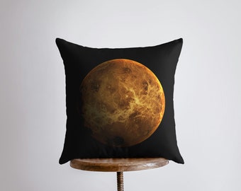 May include: A black throw pillow with a large, golden-brown image of Venus, the planet, in the center.