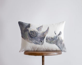 May include: A white pillow with a watercolor painting of a mother and baby rhinoceros. The mother rhino is facing the left and the baby rhino is facing the right. Both rhinos are black with gray accents.