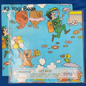 May include: A blue and green gift wrap featuring Yogi Bear and Ranger Smith from the cartoon series. The wrap features a blue background with white clouds and yellow flowers. The text on the wrap reads "Gift Wrap" and "Juvenile".
