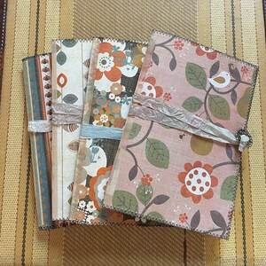May include: Four fabric-covered journals with different floral patterns. The journals are stacked on top of each other and have a rustic, vintage aesthetic.