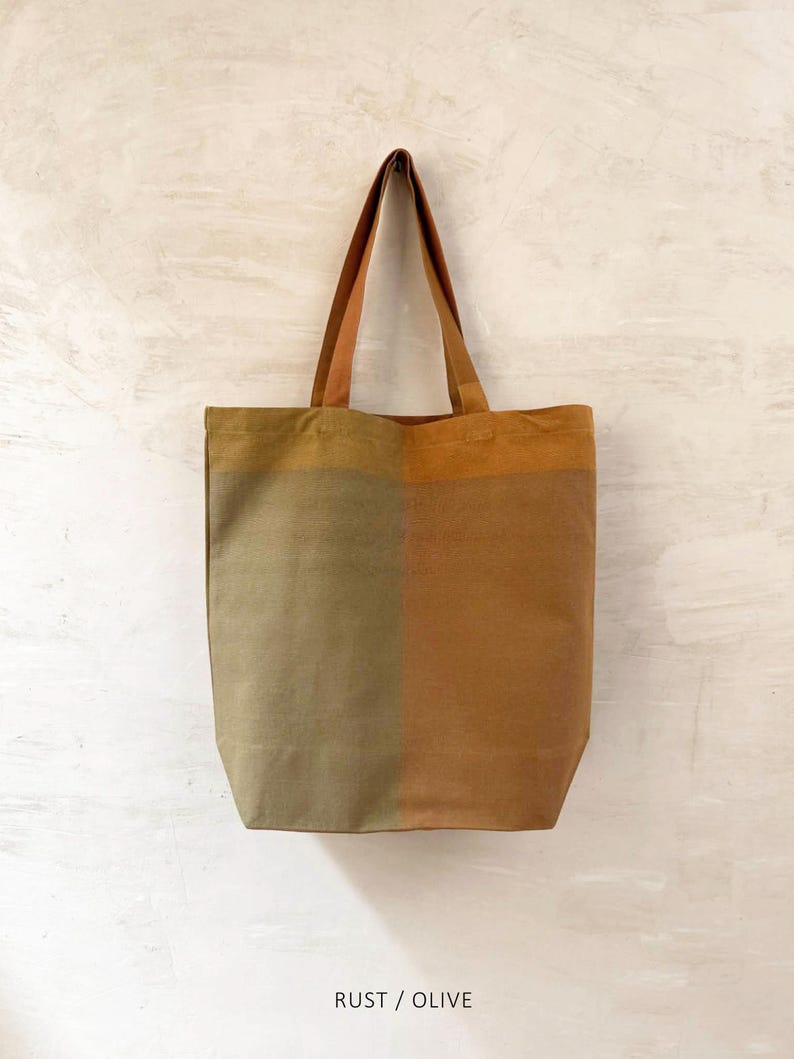 K&ouml;nnte beinhalten: Eine zweifarbige Tragetasche in Rost- und Olivgr&uuml;n. Die Tasche hat eine rechteckige Form mit flachem Boden und zwei langen Henkeln. Der Text "RUST / OLIVE" ist unten im Bild aufgedruckt.