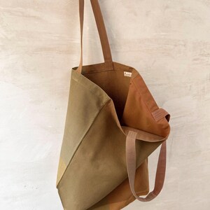 K&ouml;nnte beinhalten: Eine Tragetasche aus Segeltuch in Olivgr&uuml;n und Braun mit langen, braunen Tr&auml;gern. Die Tasche ist offen und zeigt das Innere. Die Tasche hat ein schlichtes, minimalistisches Design, das sich zum Tragen von Lebensmitteln oder Alltagsgegenst&auml;nden eignet.