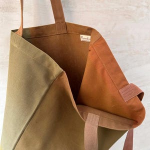 K&ouml;nnte beinhalten: Offene Canvas-Tragetasche in Olivgr&uuml;n- und Braunt&ouml;nen. Der Innenraum ist warmbraun und die Tr&auml;ger sind hellbraun. Die Tasche hat ein Etikett mit der Aufschrift "sunbird".