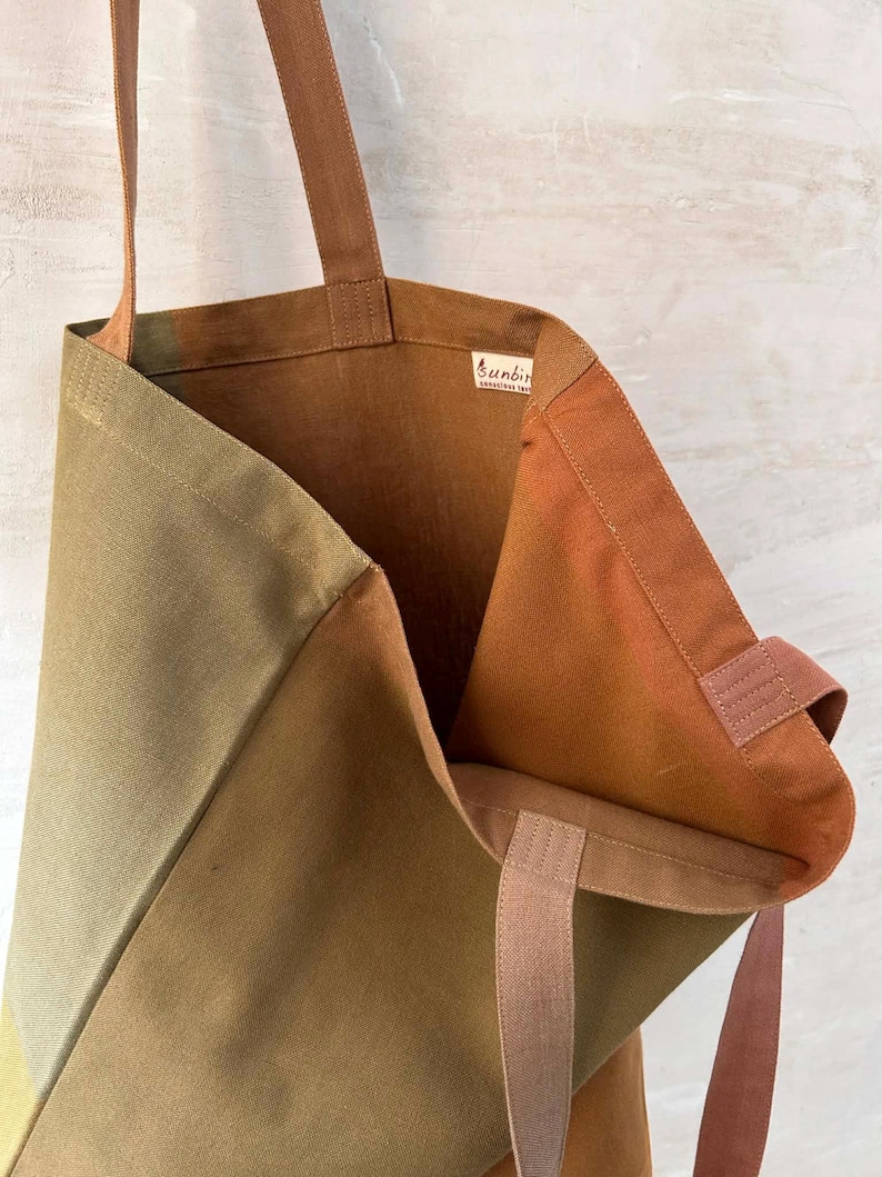 K&ouml;nnte beinhalten: Offene Canvas-Tragetasche in Olivgr&uuml;n- und Braunt&ouml;nen. Der Innenraum ist warmbraun und die Tr&auml;ger sind hellbraun. Die Tasche hat ein Etikett mit der Aufschrift "sunbird".