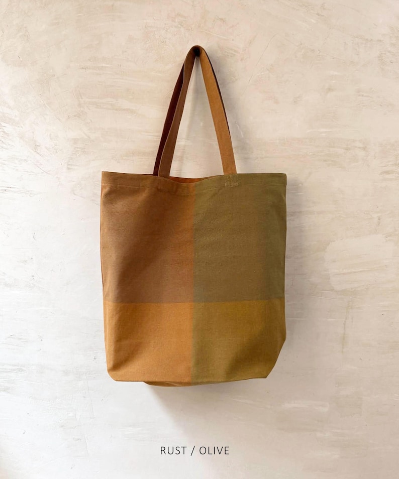 K&ouml;nnte beinhalten: Eine rechteckige Tragetasche mit einem Farbblockdesign in Rost- und Olivt&ouml;nen. Die Tasche hat lange, braune Henkel und den Text "RUST / OLIVE" unten. Die Tasche ist aus einem robusten Stoff gefertigt.