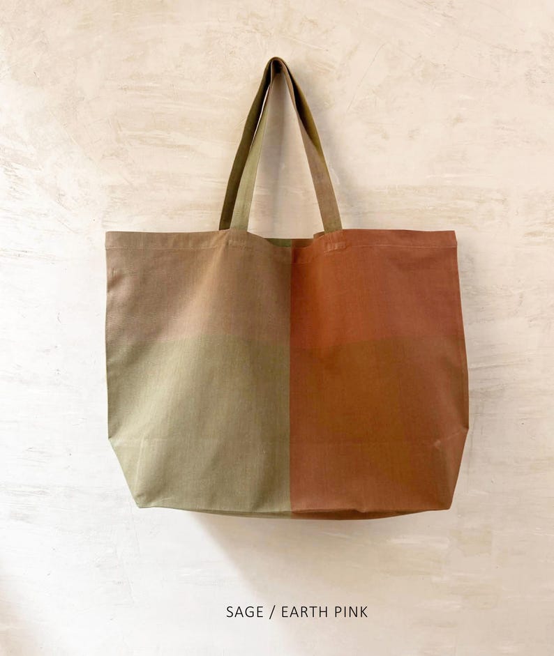 K&ouml;nnte beinhalten: Eine gro&szlig;e Tragetasche mit zweifarbigem Design. Eine Seite ist salbeigr&uuml;n, die andere erdfarbenes Rosa. Die Tasche hat passende salbeigr&uuml;ne Griffe und den Text "SAGE / EARTH PINK" unten.