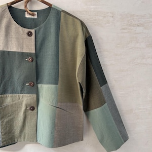 Könnte beinhalten: Eine Patchworkjacke mit Rundhalsausschnitt und langen Ärmeln. Die Jacke ist aus verschiedenen Grüntönen gefertigt und hat vier braune Knöpfe an der Vorderseite.