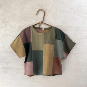 Peut inclure: Un haut patchwork avec un col rond et des manches courtes. Le haut est fait de tissus de différentes couleurs, dont le marron, le vert et le rose.