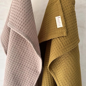 May include: Two waffle weave kitchen towels, one in a light brown color and one in a mustard yellow color. The yellow towel has a small label that says "Sunbird" on it.