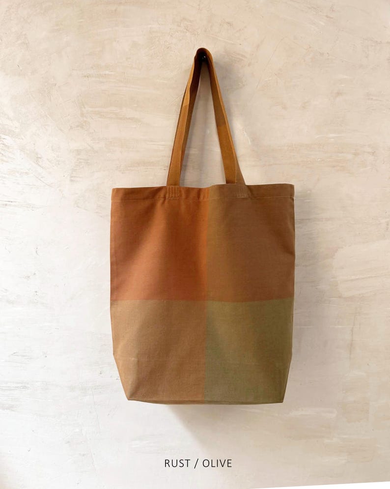 K&ouml;nnte beinhalten: Eine rechteckige Tragetasche in Rost- und Olivgr&uuml;n. Die Tasche ist in vier farbblockierte Abschnitte unterteilt. Sie hat zwei lange Henkel und der Text "RUST / OLIVE" ist unten aufgedruckt.