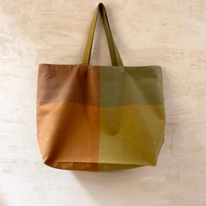 K&ouml;nnte beinhalten: Eine gro&szlig;e Tragetasche mit einem Farbblock-Design in Rost- und Olivgr&uuml;n. Die Tasche hat eine rechteckige Form mit passendem Griff. Der Text "RUST / OLIVE" ist am unteren Rand des Bildes aufgedruckt.
