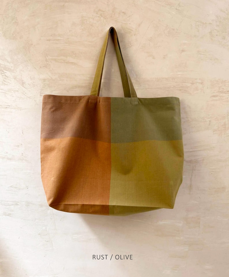 K&ouml;nnte beinhalten: Eine gro&szlig;e Tragetasche mit einem Farbblock-Design in Rost- und Olivgr&uuml;n. Die Tasche hat eine rechteckige Form mit passendem Griff. Der Text "RUST / OLIVE" ist am unteren Rand des Bildes aufgedruckt.