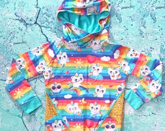 May include: A turquoise blue hooded sweatshirt with a rainbow stripe pattern and a graphic print of cartoon cats. The sweatshirt has a gold glitter pocket on the side.