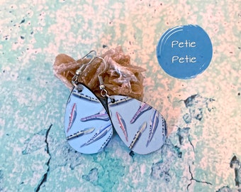 May include: A pair of teardrop-shaped earrings with a blue background and a pattern of colourful feathers. The earrings are made of wood and have silver hooks.