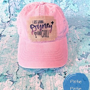 May include: Pink baseball cap with a brown patch that says "I just wanna Disney and chill" with a wine glass icon.