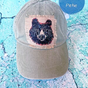May include: A green baseball cap with a brown patch featuring a black bear with sunglasses and the text "Mama Bear".