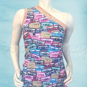 May include: A sleeveless, one-shoulder top with a colorful print of cassette tapes. The top has a gold sequined trim along the neckline.