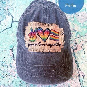 May include: A dark blue denim baseball cap with a patch that says "peace love equality" and features a peace sign, a heart, and a rainbow flag.