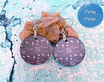 May include: A pair of silver dangle earrings with round black and white Harry Potter themed charms. The charms feature a repeating pattern of lightning bolts, broomsticks, and the Harry Potter logo.