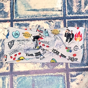 Puede incluir: Una diadema de tela gris claro con un patrón repetido de varios gráficos y texto. El diseño incluye imágenes de un reproductor de casetes, un corazón, un pájaro y las palabras "WAFFLE HOUSE", "LOVEBUG" y "YEAR 3000".