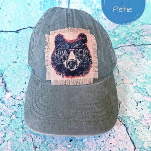 May include: A dark green baseball cap with a brown burlap patch featuring a black bear wearing sunglasses and the text "Mama Bear".
