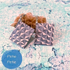 May include: A pair of silver geometric earrings with a grey and white pattern. The earrings are square shaped and have a 3D effect.