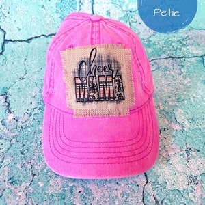May include: Pink baseball cap with a brown burlap patch that says "Cheer Mom" in black cursive lettering. The patch has a plaid and leopard print design.